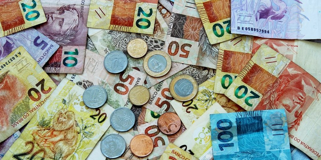 Cédulas e moedas de real espalhadas sobre uma mesa.