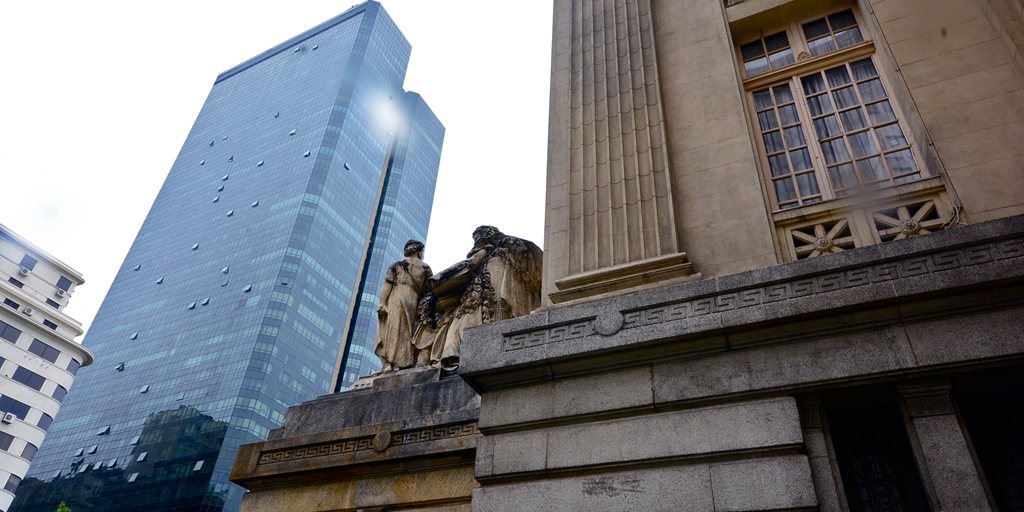 Torre de escritórios espelhada ao lado de um edifício histórico no centro do Rio de Janeiro.
